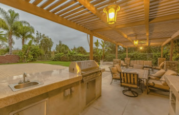 outdoor kitchen and dining area under a pergola at the spacious patio of a home